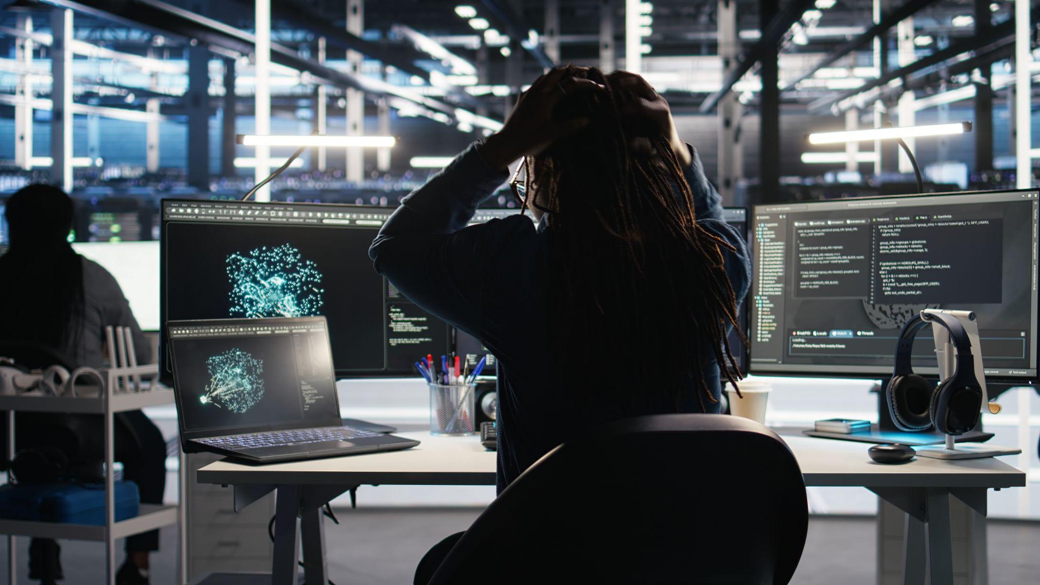 Woman looking at screens experiencing IT downtime.
